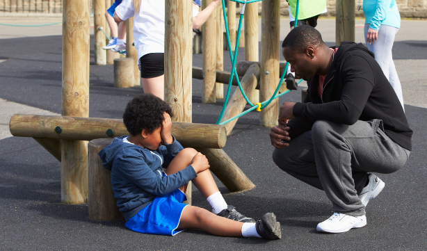 Photo of a parent talking with a child on a playground.