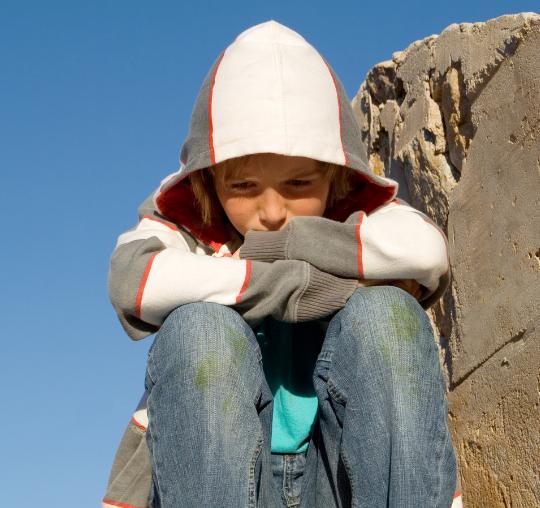 Photo of a boy with a hoodie and grass stains looking sad.